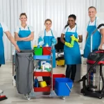 Group of happy cleaners standing with cleaning equipments in office