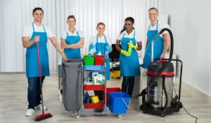 Group of happy cleaners standing with cleaning equipments in office