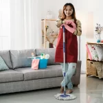 female housekeeper standing with keeping her arms on the mop in a bright home interior