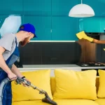man with vacuum cleaner washing with vapor yellow sofa and woman wipes furniture