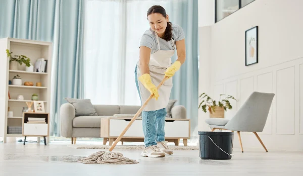 Woman cleaning the floor with a mop in the living room in home with a smile