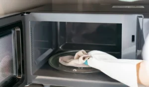 Woman hand with microfiber rag cleaning inside of microwave oven in kitchen at home. Closeup