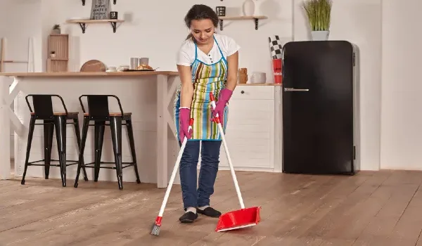 Young woman sweeping floor on the kitchen