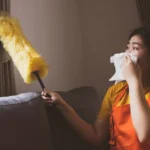 Asian woman doing housework dusting dirty window blinds covering her nose allergy