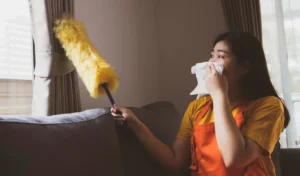 Asian woman doing housework dusting dirty window blinds covering her nose allergy