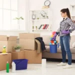 Young woman tiding up after moving to new appartment. Girl with various detergents, rags and mops in living room full of carton boxes