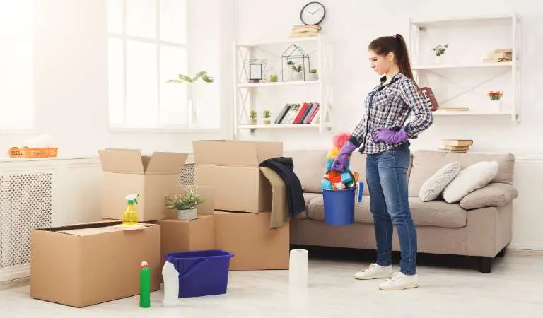 Young woman tiding up after moving to new appartment. Girl with various detergents, rags and mops in living room full of carton boxes