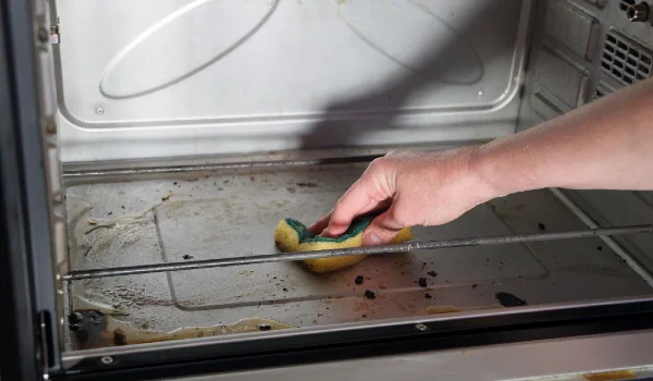 Female hand with sponge and detergent cleaning the kitchen oven from burnt drops