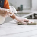 Person wearing gloves when cleaning marble counter with disinfectant spray and cloth