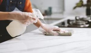 Person wearing gloves when cleaning marble counter with disinfectant spray and cloth