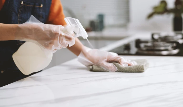 Person wearing gloves when cleaning marble counter with disinfectant spray and cloth