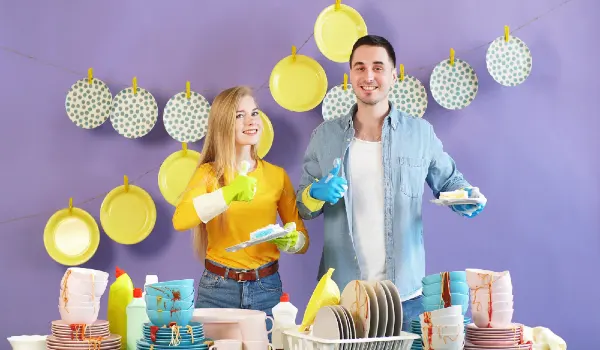 Positive young woman and a black-haired man give a thumbs up while holding clean plates. Clean plates hang on clothespins in the background
