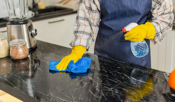 Woman wiping kitchen marble counter with disinfectant spray for daily clean home hygiene in apartment