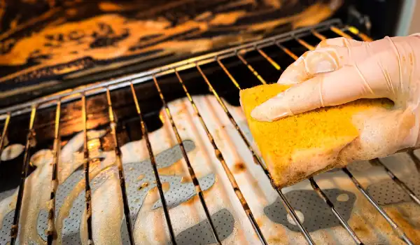 Cleaning the oven from heavy grease in the kitchen hand in a household glove and with a yellow sponge