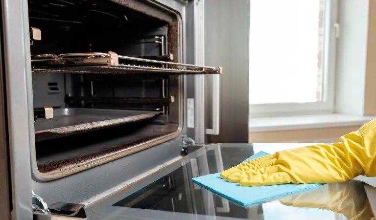 Man with rag and rubber gloves cleaning kitchen oven